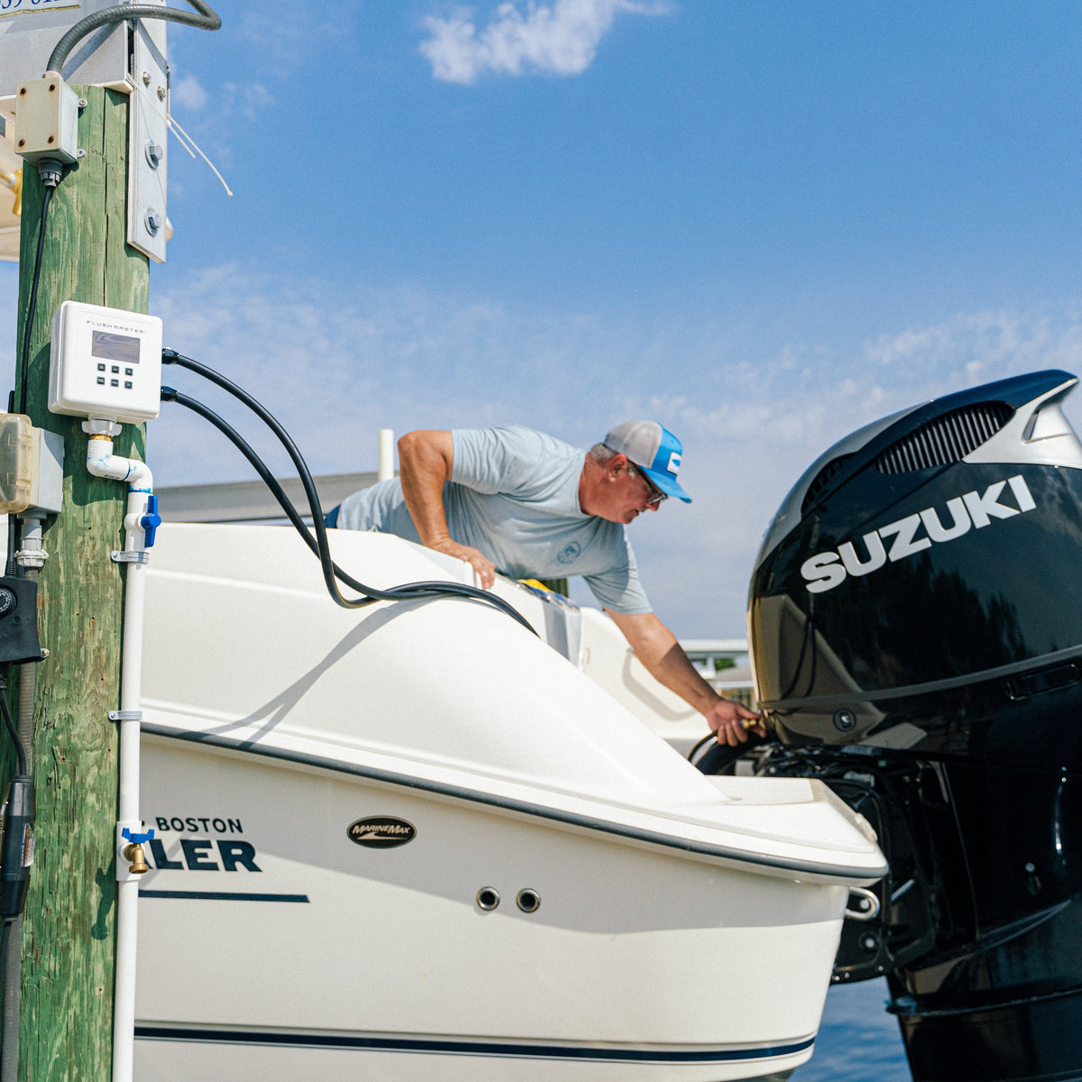 Boater connecting a flushing hose to a Suzuki outboard beside a dock-mounted Flushmaster Controller.