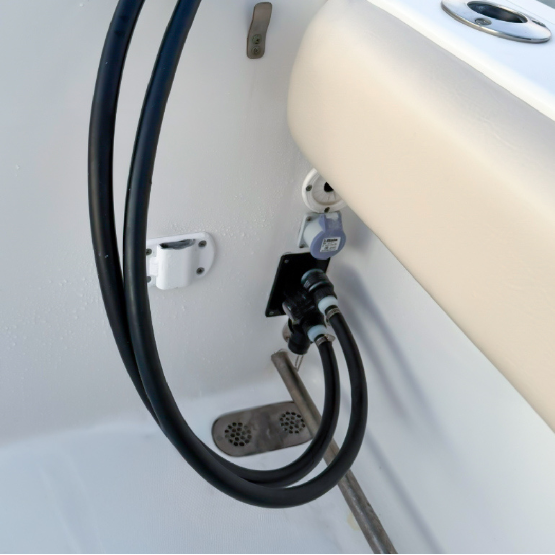 Two black flushing hoses with hose-side adapters attached to a vertical black dual Reroute plate inside a boat.