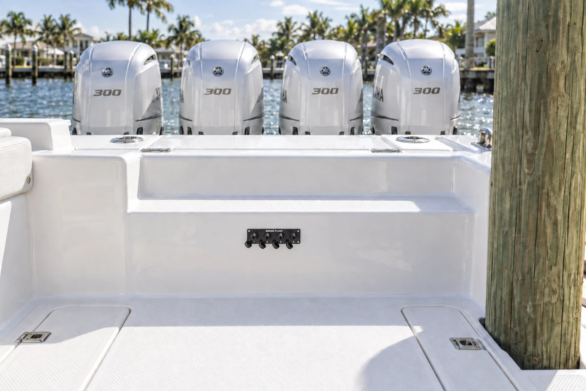 Illustrated black quad Flush Port Reroute plate mounted horizontally on the aft cockpit step, with open tethered locking caps and four outboards behind the transom