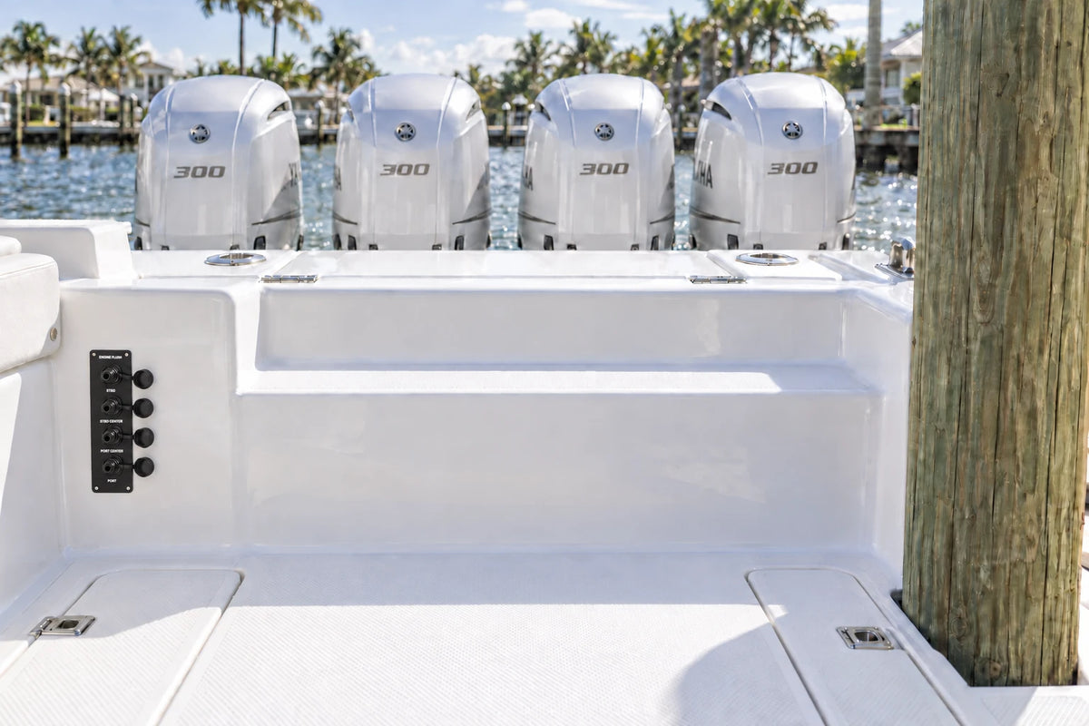 Illustrated black quad Flush Port Reroute plate mounted vertically below the boat side bolster, with open tethered locking caps and four outboards behind the transom