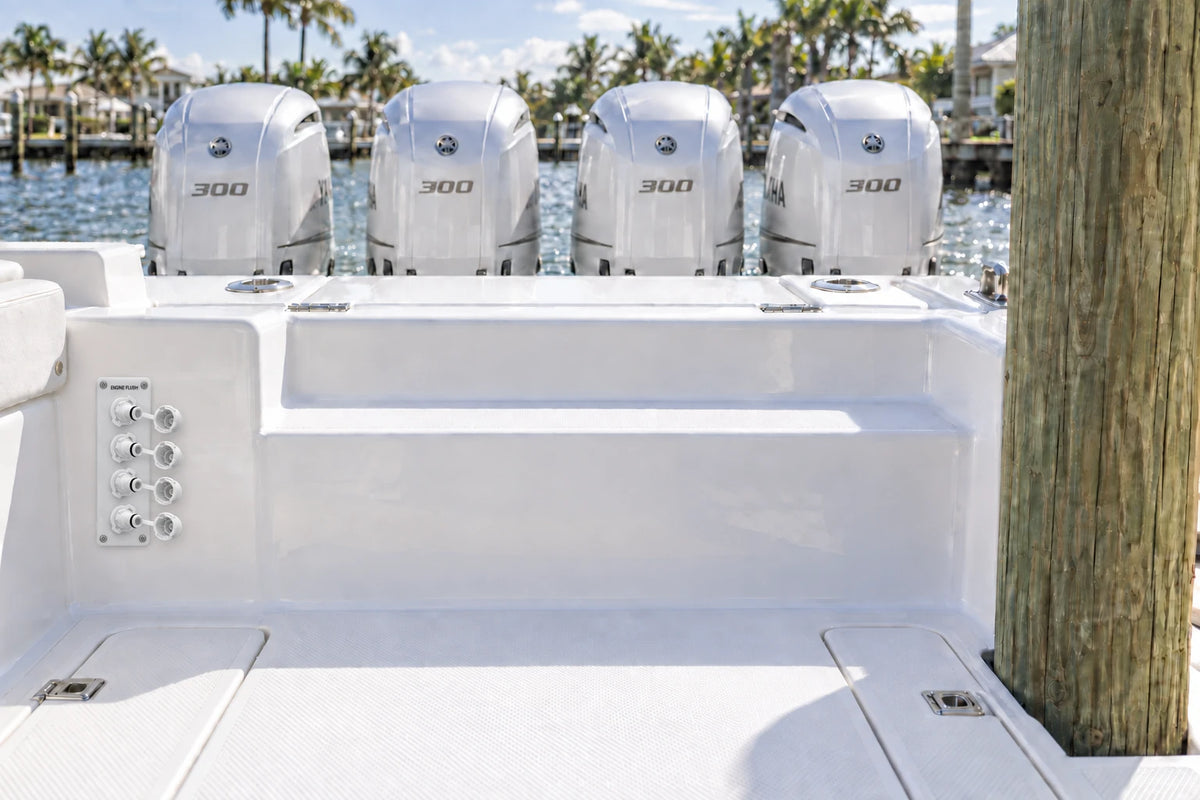 Illustrated white quad Flush Port Reroute plate mounted vertically below the boat side bolster, with open tethered locking caps and four outboards behind the transom